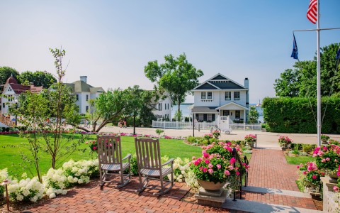 chairs on a brick walkway with flowers in front of a house