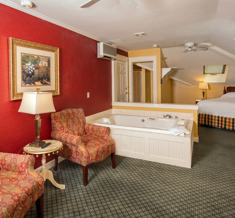 View of a big room with a private jacuzzi a large bed and some arm chairs