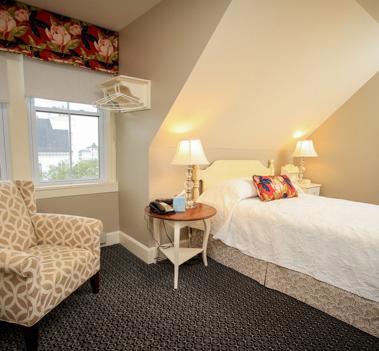 View of a single bed next to an elegant armchair and a nightstand