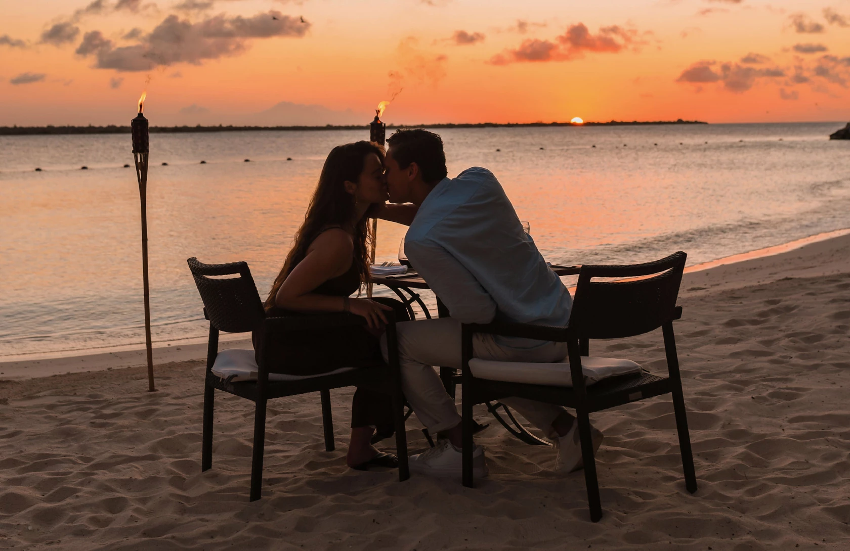 a man and woman sitting at a table on a beach