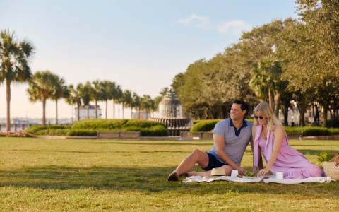 a man and woman sitting on a blanket in a park