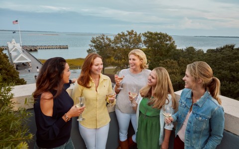 a group of women standing on a ledge with wine glasses