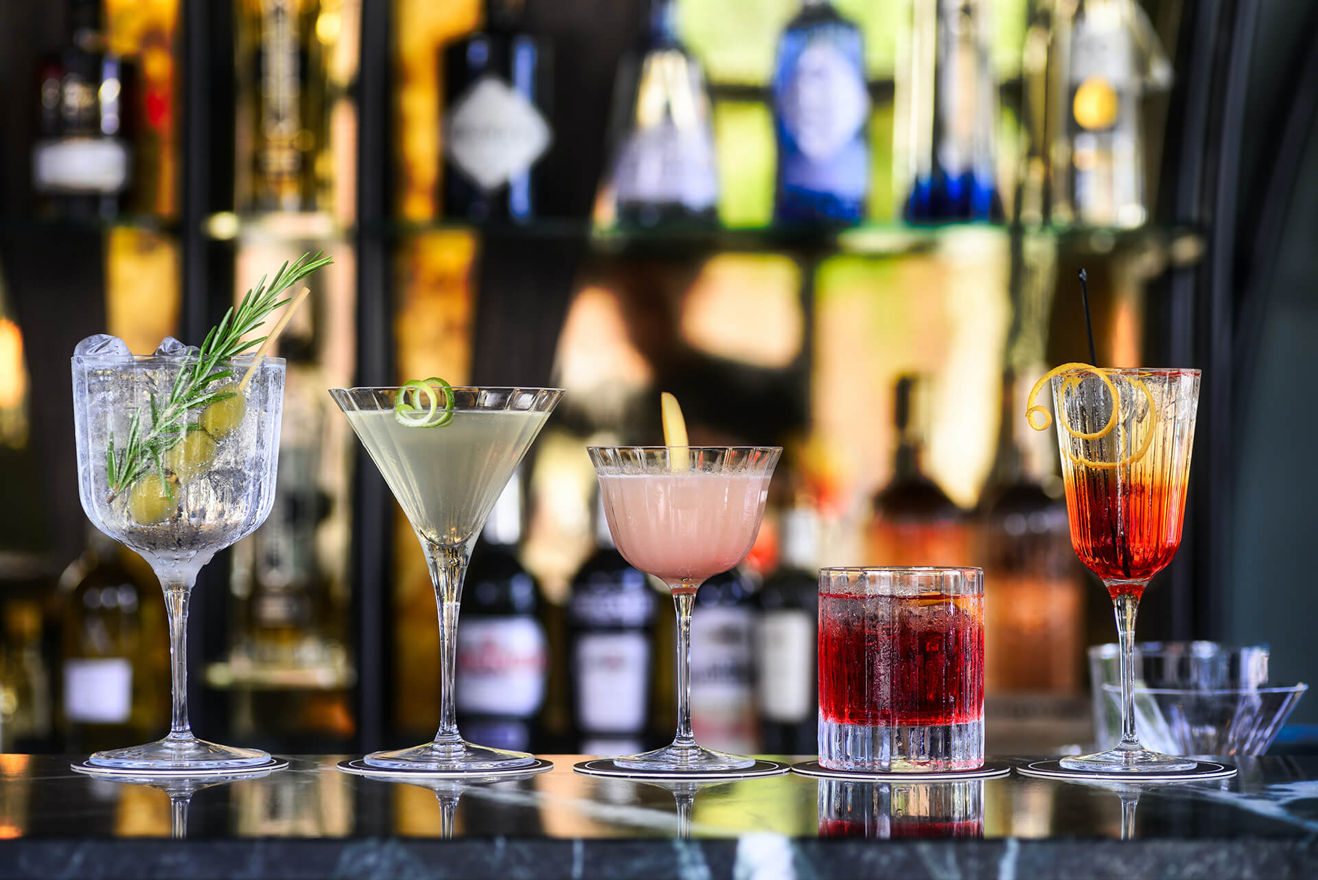 five cocktails on a bar with liquor in the background