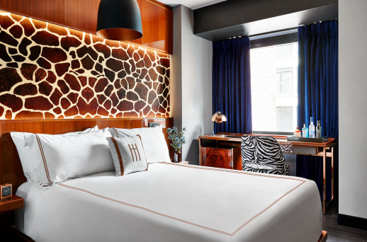 A hotel room with a king-sized bed, desk, chair, and window