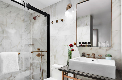 A modern bathroom with marble tiles, a glass-enclosed shower, and a white sink under a large mirror.