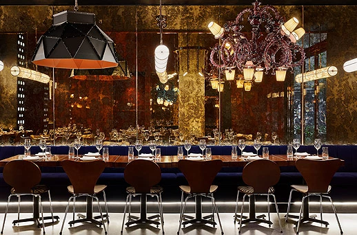 A formal dining area with a long table, blue booth seating, and multiple chandeliers.