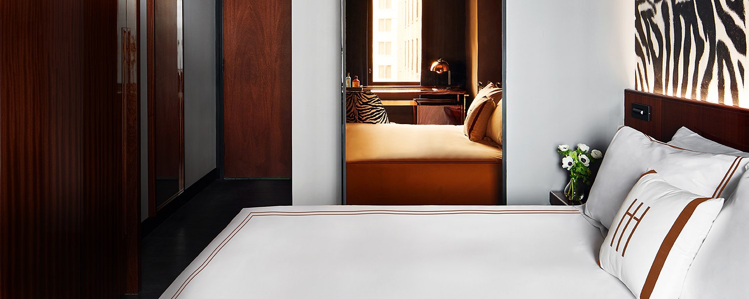 A close-up of a bed with white bedding and brown accents, with a vase of flowers on a nightstand.