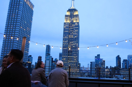 A group of people on a rooftop with a view of the city skyline at dusk.