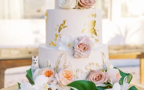 Large white wedding cake surrounded by pink flowers and green leaves.