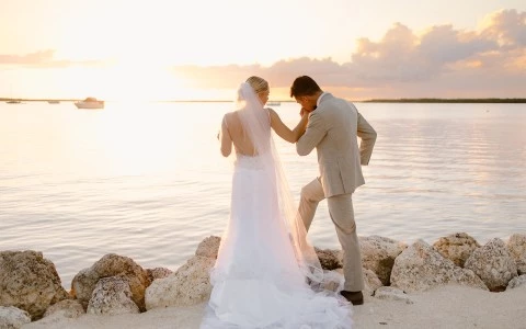 a man and woman in wedding attire kissing on a rocky beach