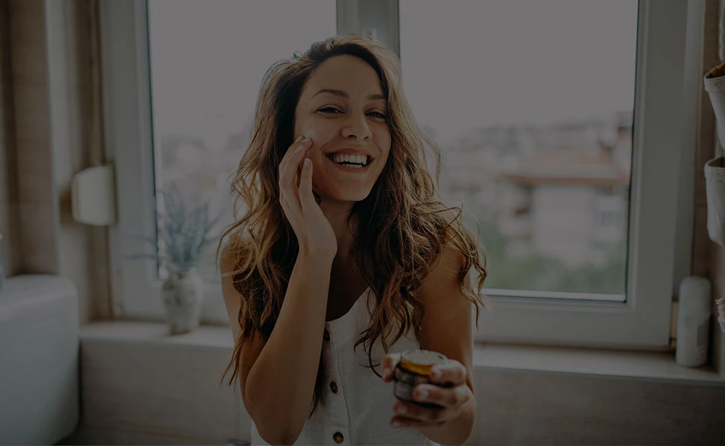 woman sitting down and rubbing a cream onto her cheek