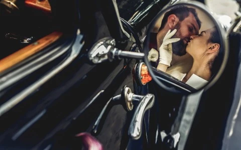 Reflection of wedding couple kissing through car side view mirror