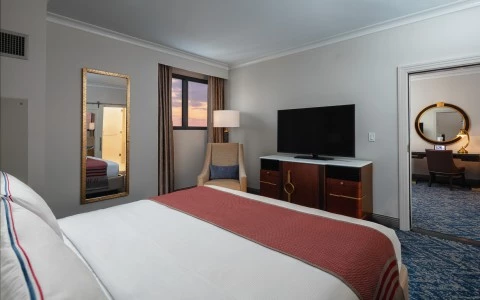 bedroom with double bed, a tv, a sided wall mirror showing behind a desk and a rounded mirror 24