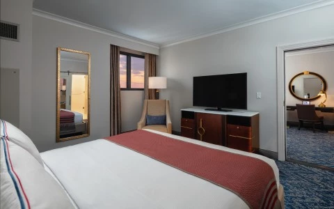 bedroom with double bed, a tv, a sided wall mirror showing behind a desk and a rounded mirror 23
