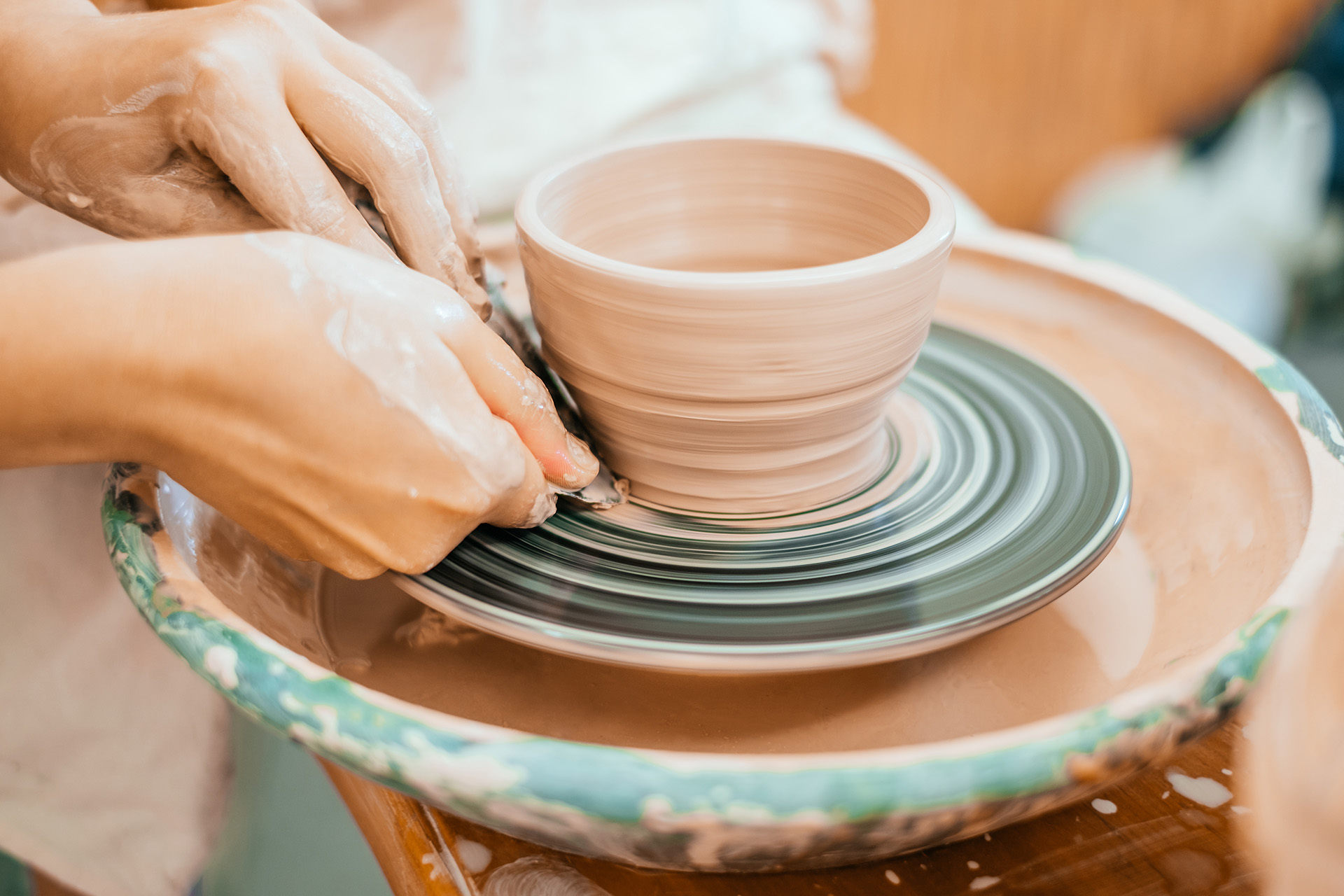 a person's hands painting a clay cup on a pottery wheel
