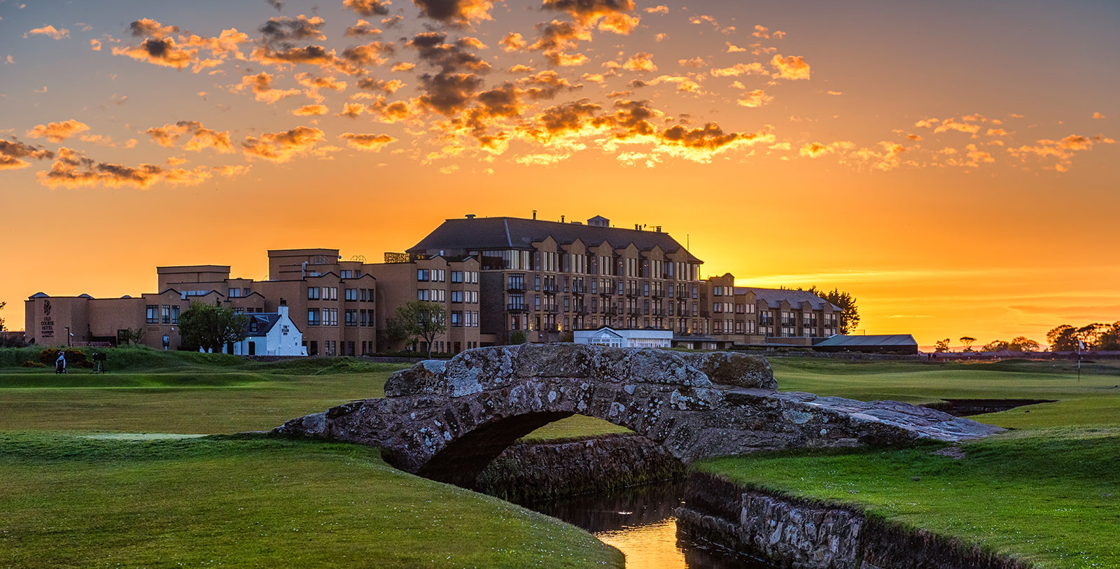 a bridge over a river in a grassy area with a building in the background