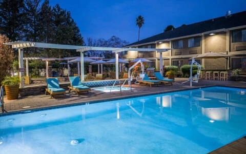 brightly lit hotel pool with lounge chair seating at night
