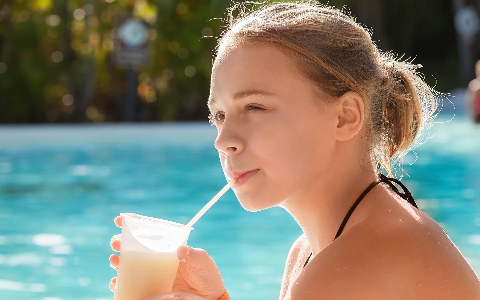 Lady sitting by the pool, dinking her beverage out of a straw