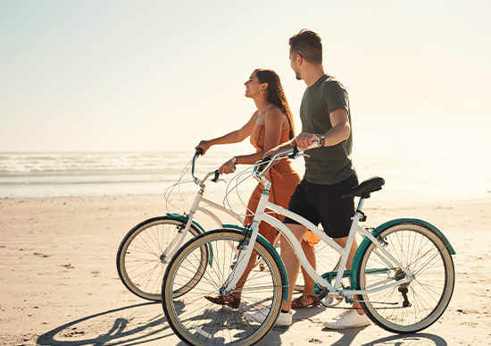Man and woman taking a walk on the beach with their bikes 