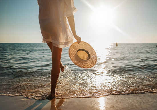 Woman splashing her feet in the ocean, holding a sombrero 