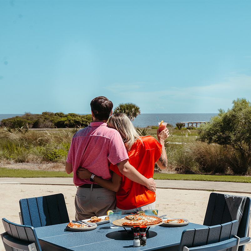 a man and woman hugging at a table with food on it