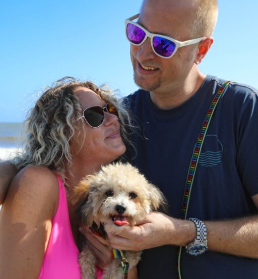 a man and woman holding a dog on a beach