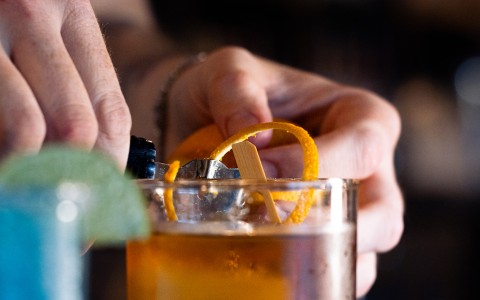 a person squeezing an orange peel into a glass of liquid