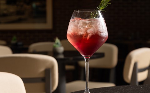 a glass of red liquid with a sprig of rosemary on a table