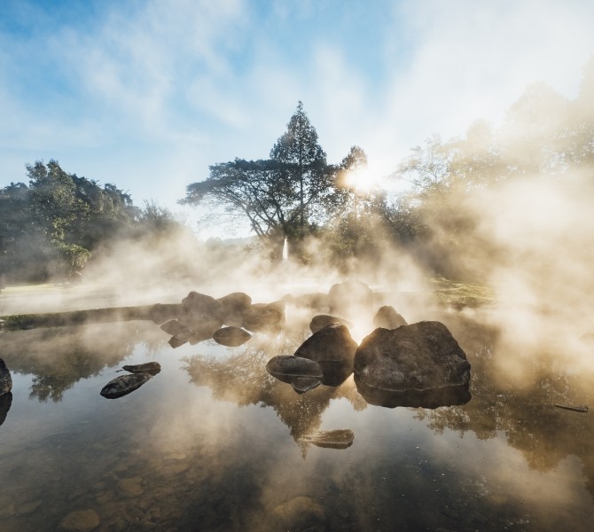 a body of water with steam and trees in the background