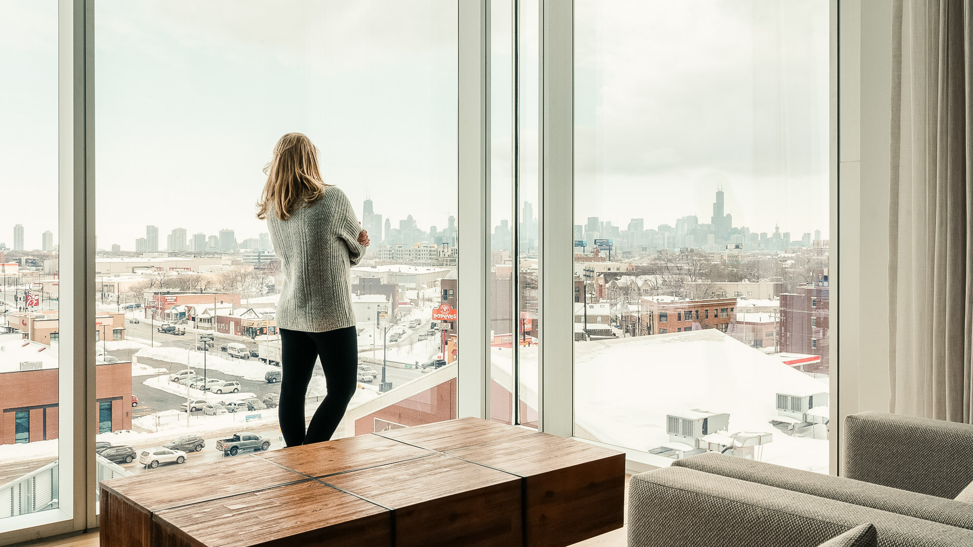 a woman standing in front of a window looking out a city