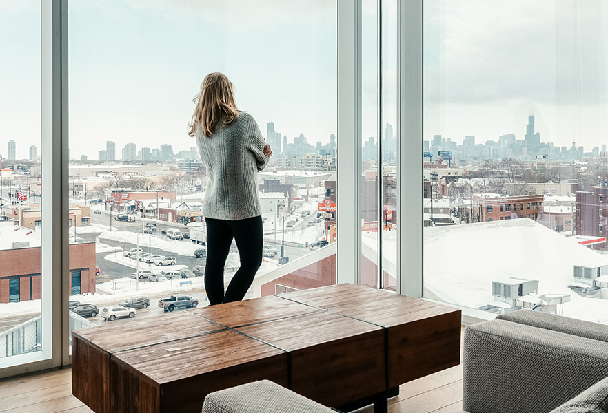 a woman standing in front of a window looking out a city