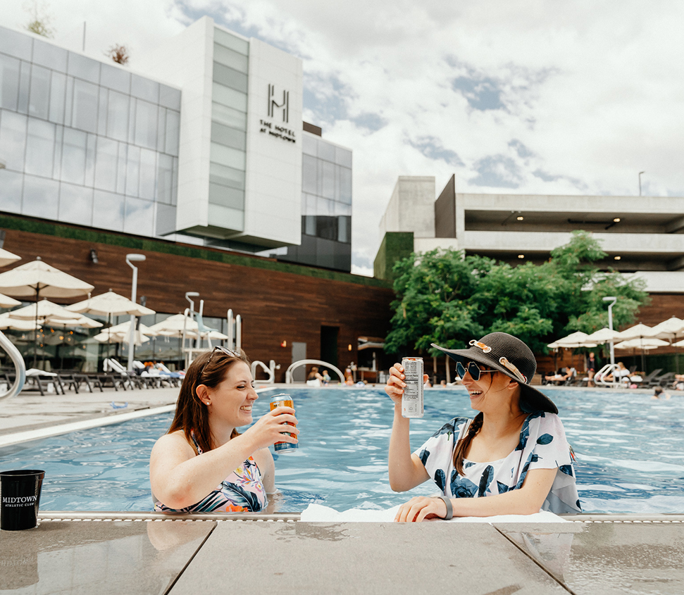 two women sitting in a pool holding drinks