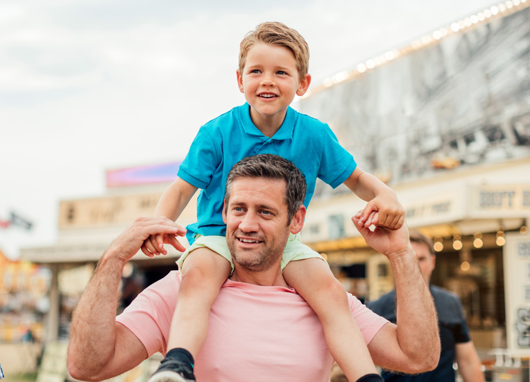 man carrying a child on his shoulders while they are walking in the street