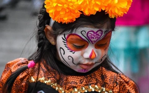 a girl with face paint and orange flowers on her head