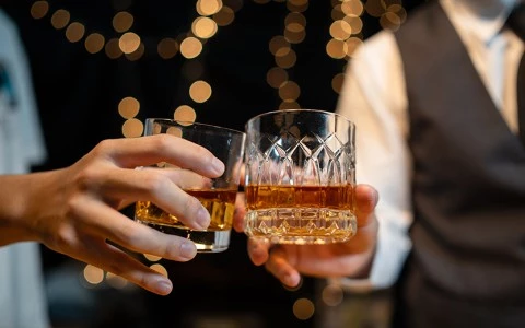 two hands holding glasses with alcohol