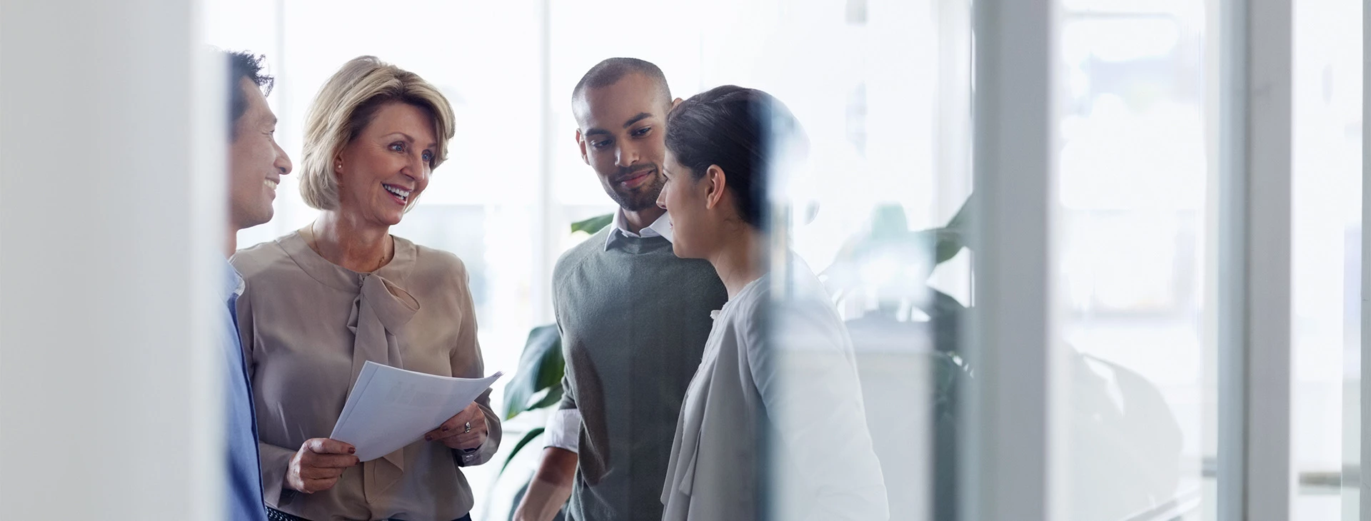 Two men and two women wearing business clothes and looking at each other while holding documents in a well lit area.