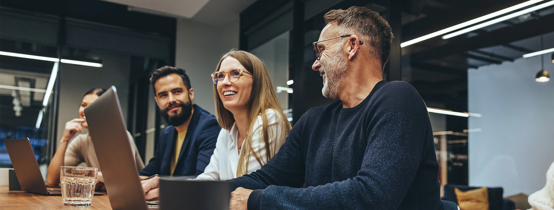 A group of smiling business people sitting in a conference room with their laptops.