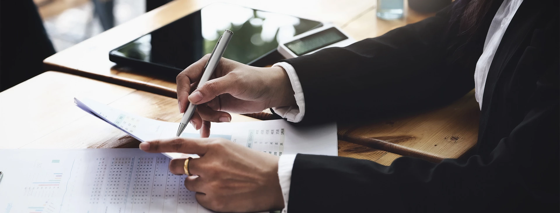 A man wearing a black suit reading a document and holding a white pen.