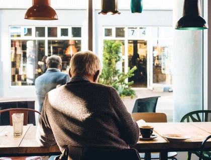 an older man sitting at a table having a cappuccino