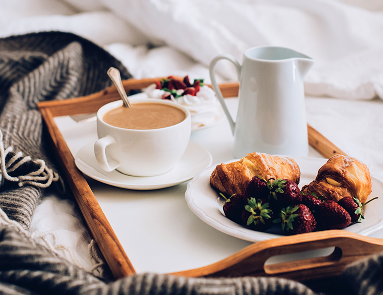 a tray in bed with a cappuccino and a croissant with fruits