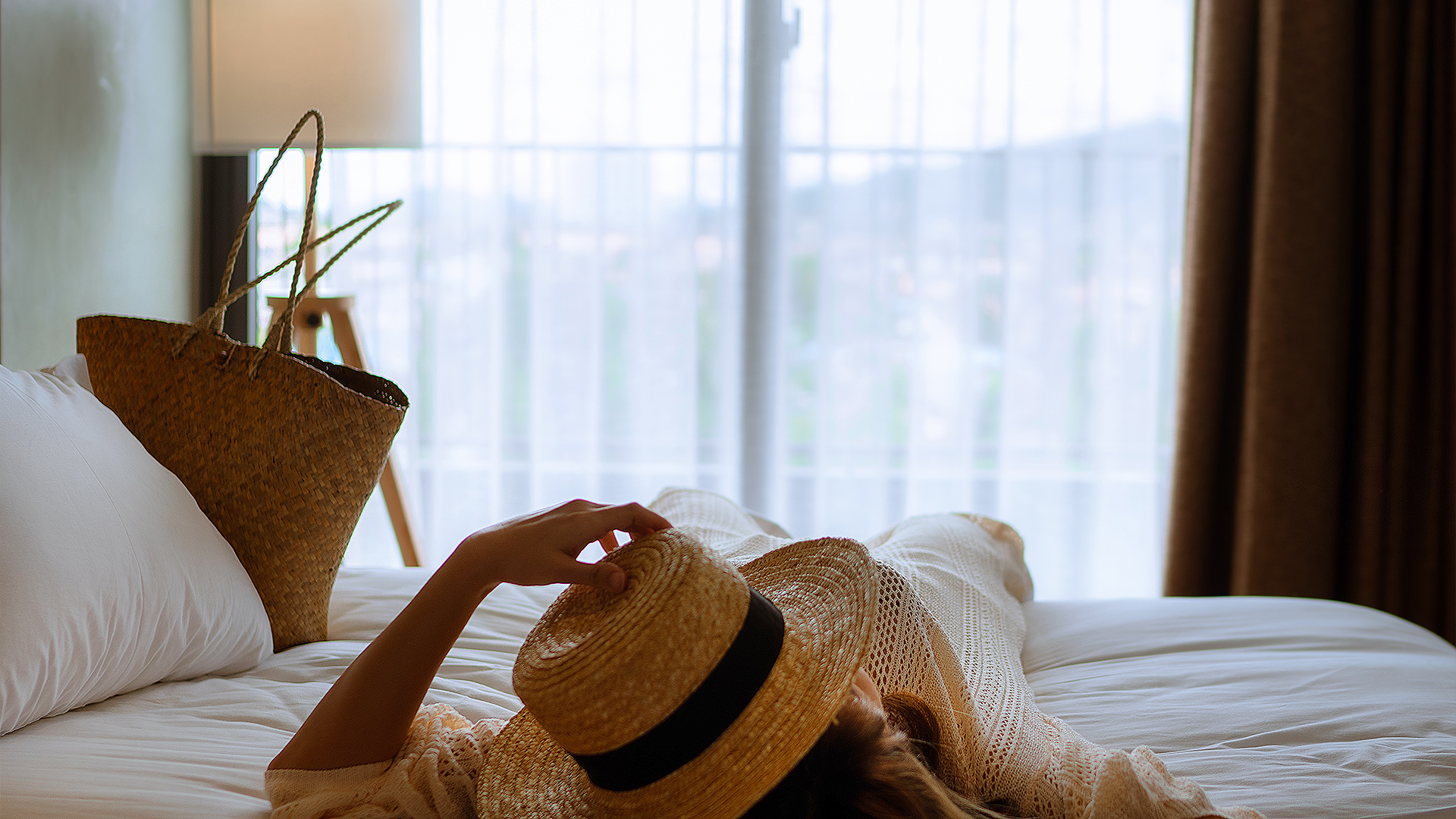 a woman lying on a bed with a straw hat