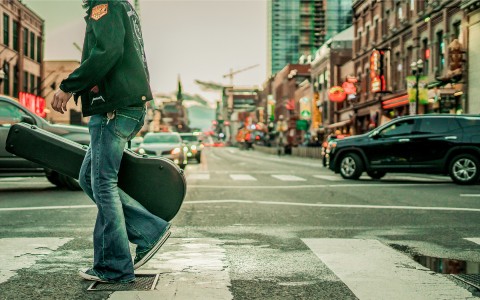 A person carrying a guitar and walking down New York streets