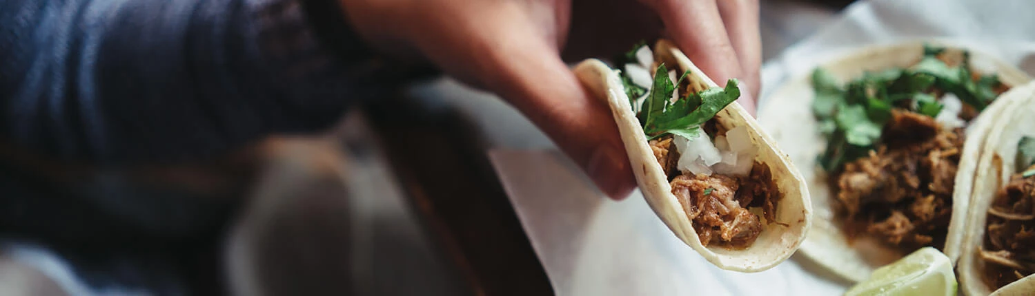 a hand holding a taco with meat, onion, and cilantro