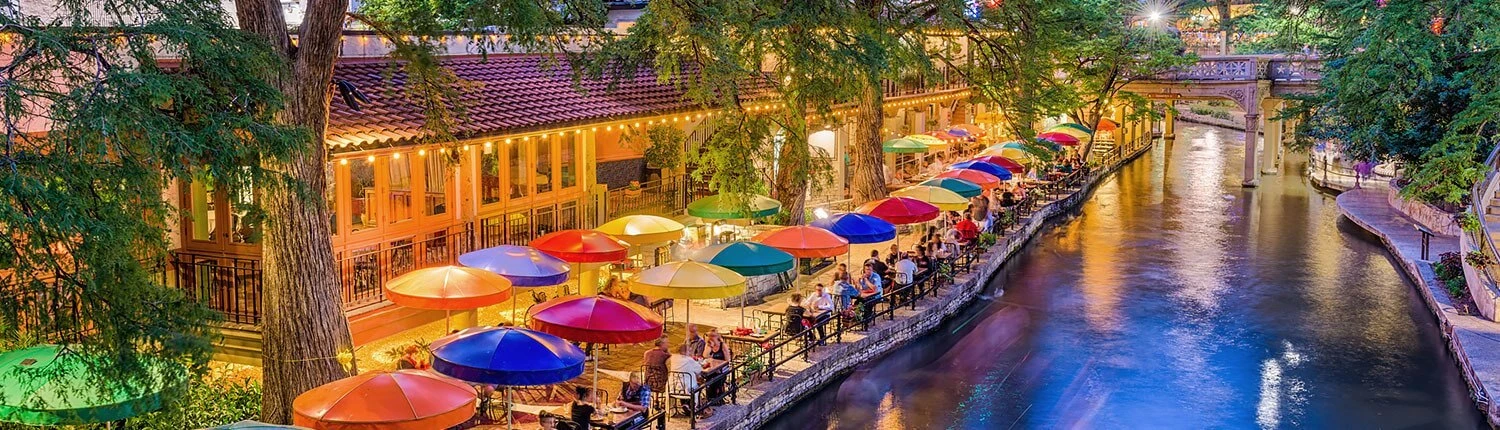 A riverwalk with colorful umbrellas and dining areas along the water