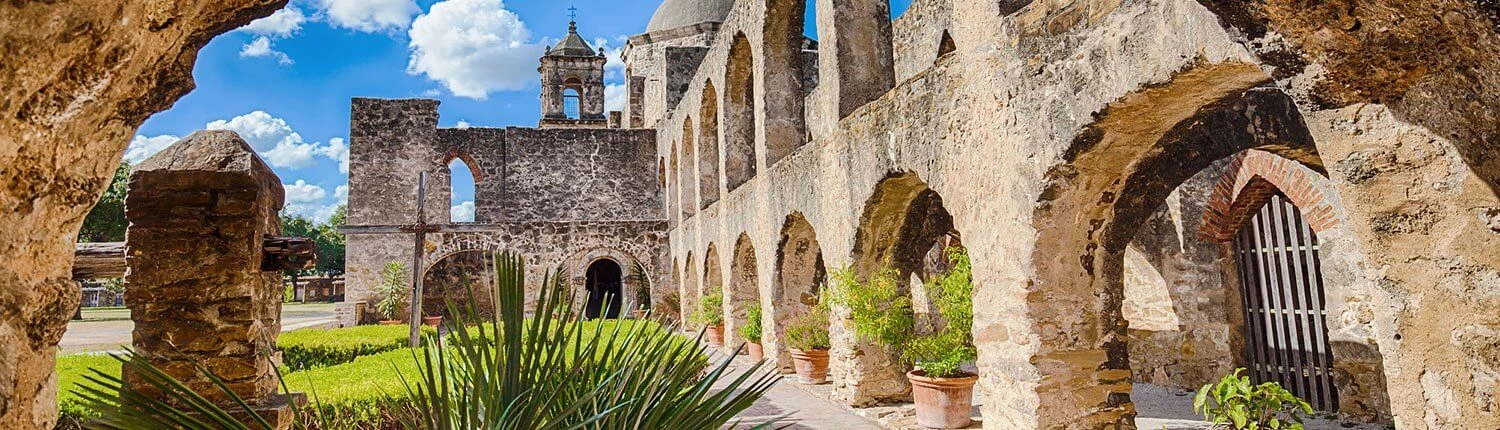 A historic stone building with arches and a tower under a blue sky.