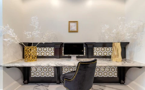 A lobby reception desk with a marble top, gold accents, and a black chair.
