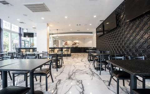 A modern dining area with black tables and chairs, a marble floor, and a decorative wall.
