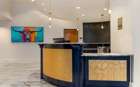 A modern hotel lobby with a curved front desk, marble floors, and a colorful bull artwork.