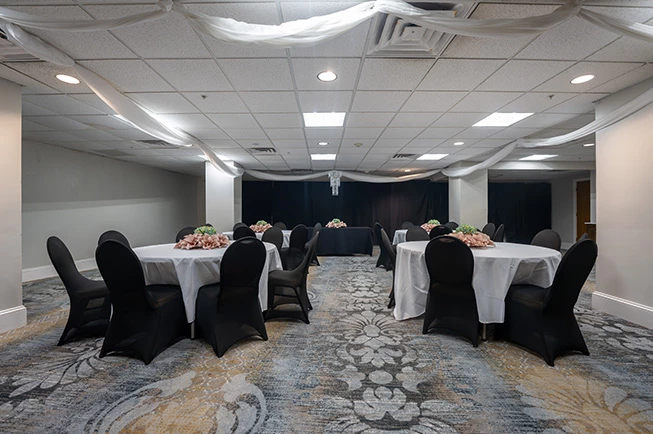 A meeting room with round tables, black chairs, floral arrangements, and ceiling draping.