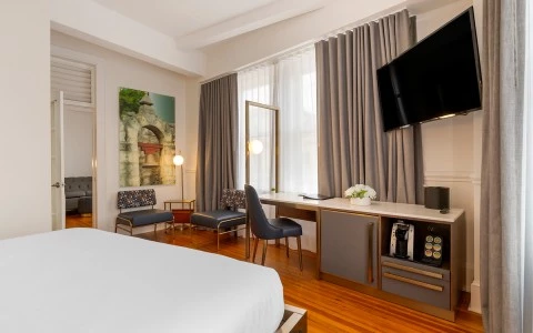 A wide view of a hotel room with a bed, desk, seating area, and TV